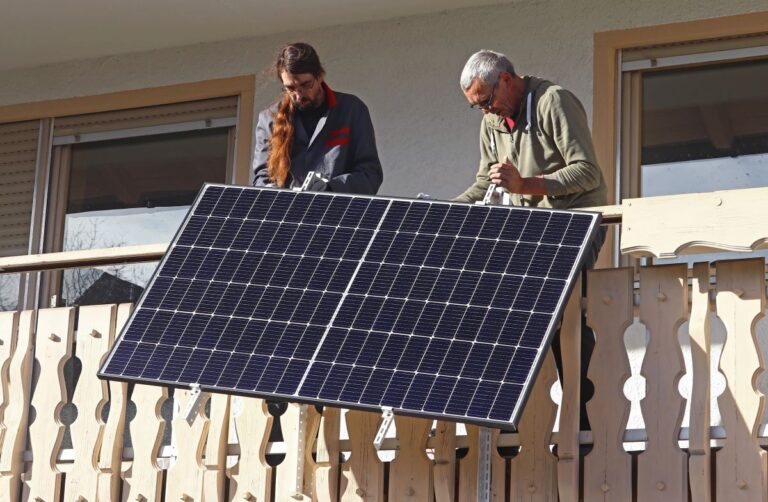 Zwei Männer montieren Solarpanel am Balkon.