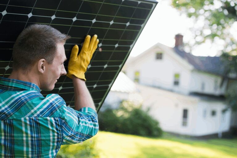Mann trägt Solarpanel vor Wohnhaus im Garten